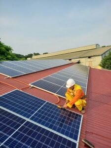 Technician working on solar panel installation on a rooftop under clear sky.