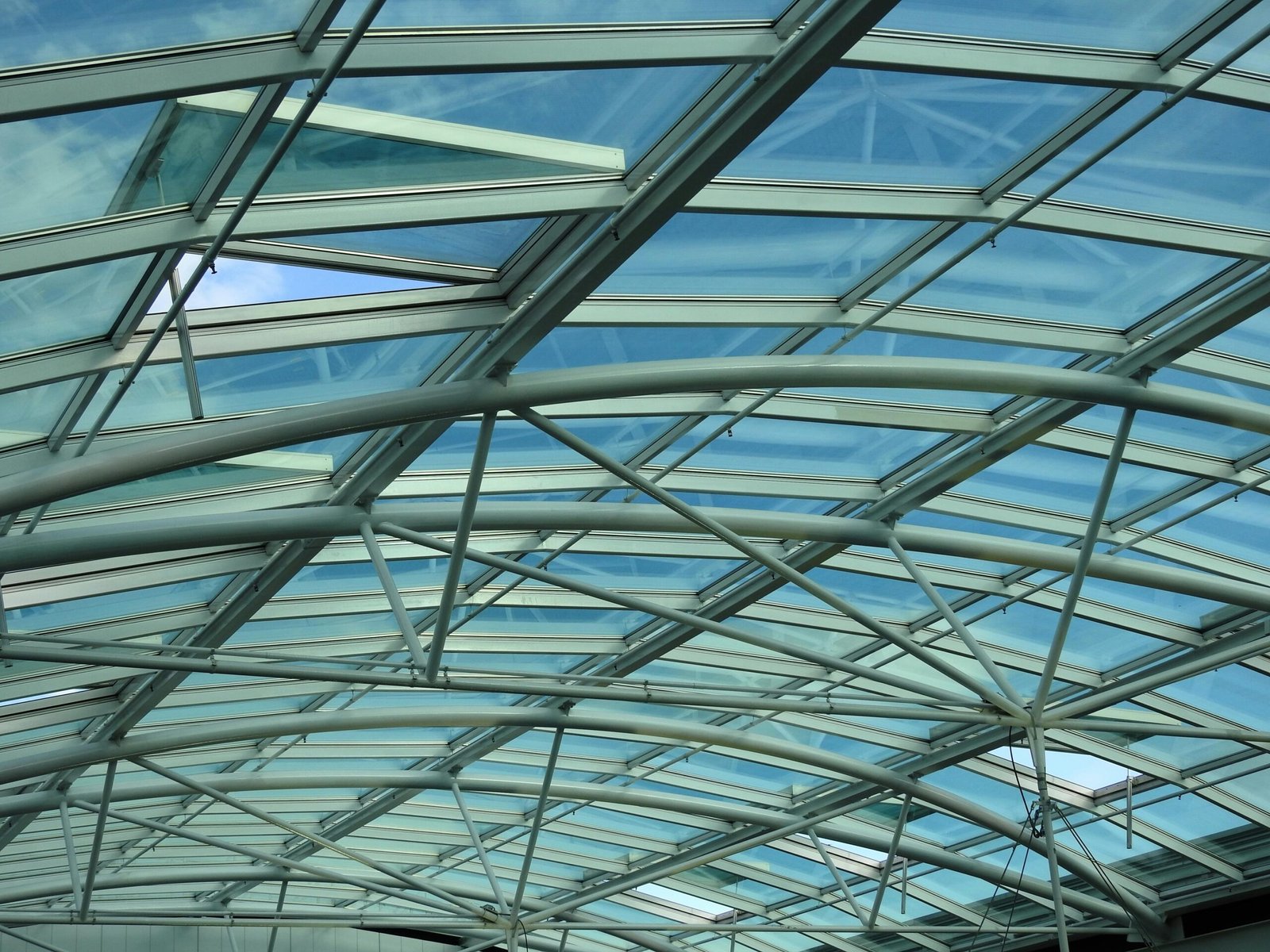 Intricate modern glass ceiling structure with blue sky visible through clear panels, highlighting architectural design.