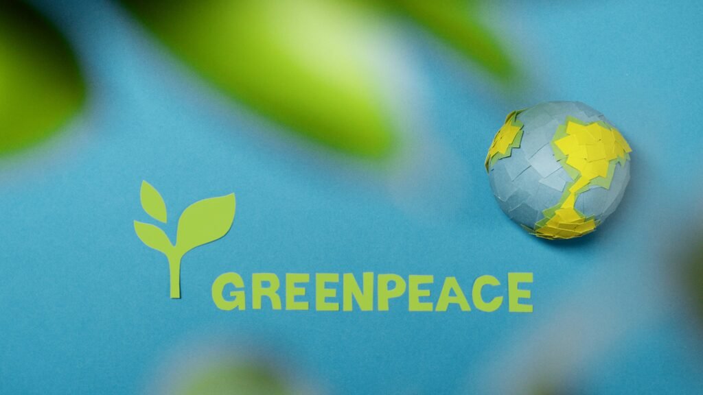 Greenpeace logo and Earth cutout on blue background symbolizing environmental awareness.